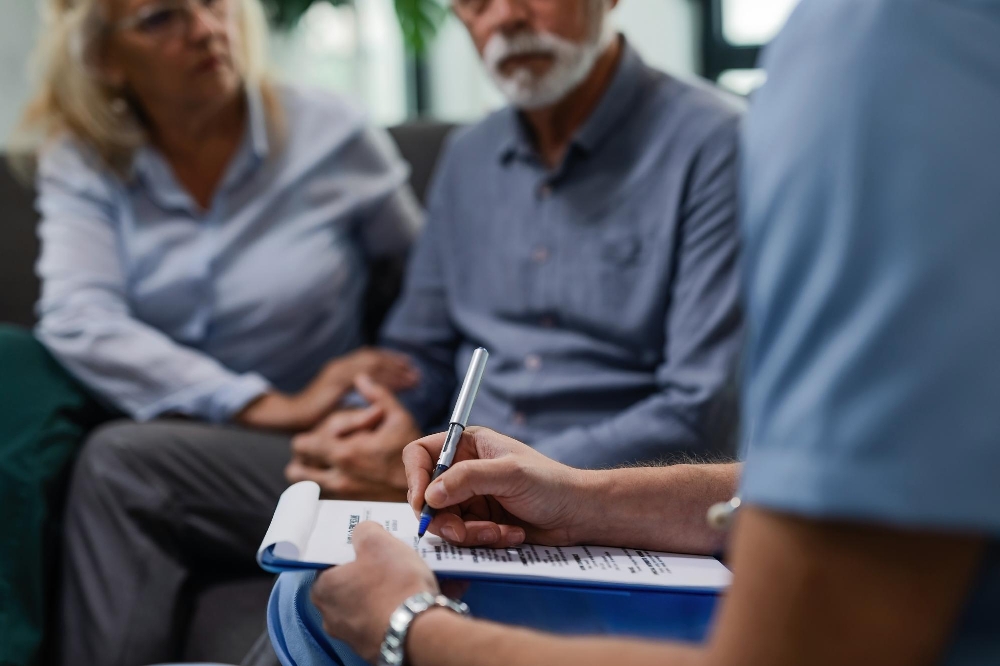 A doctor writing a medical report while visiting a senior couple at their home.